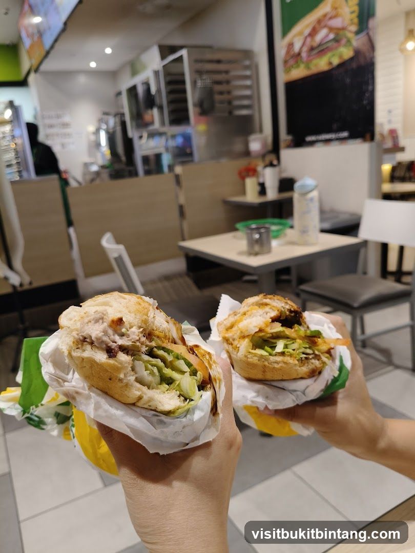 Two sandwiches held up in front of a Subway restaurant