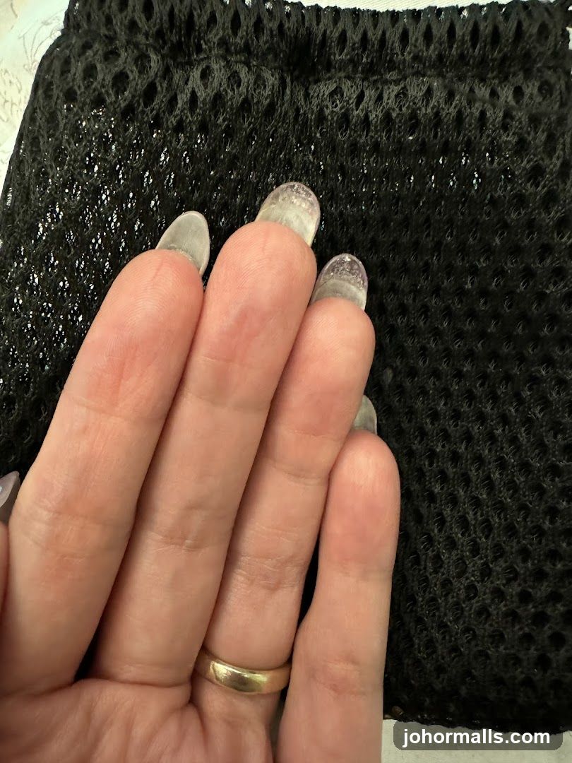Hand with transparent nail tips on black mesh background