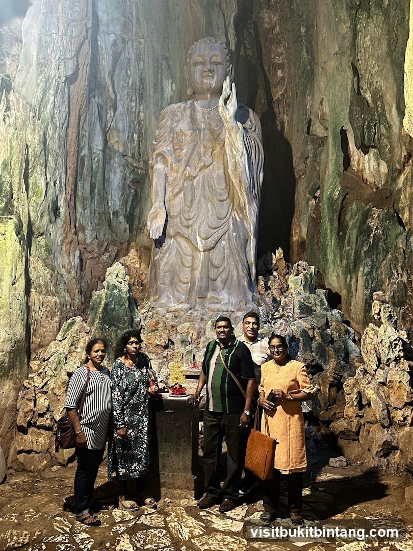 People Posing in Front of a Large Buddha Statue in a Cave