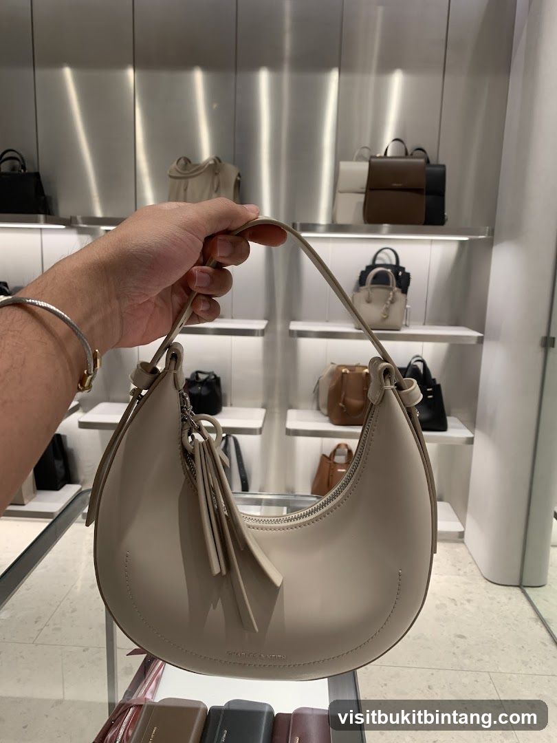 Hand holding a cream-colored crescent-shaped handbag