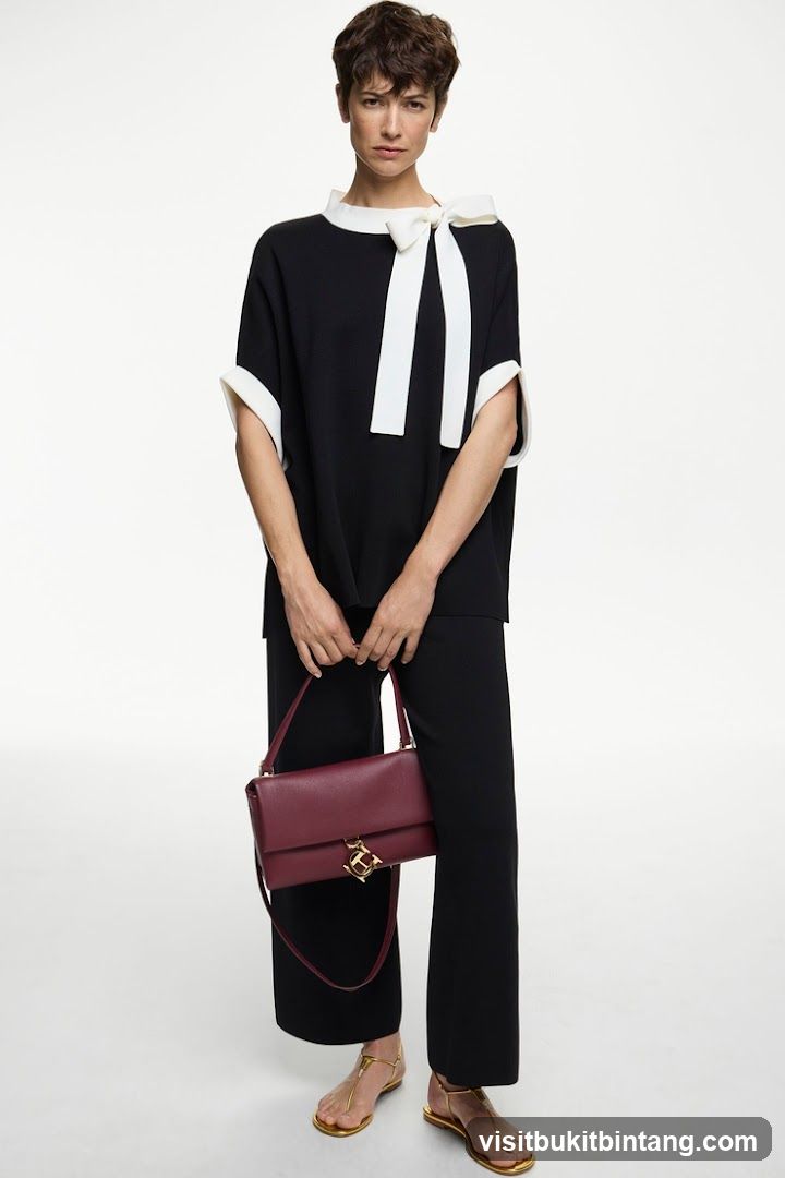 Model wearing black and white outfit with burgundy handbag