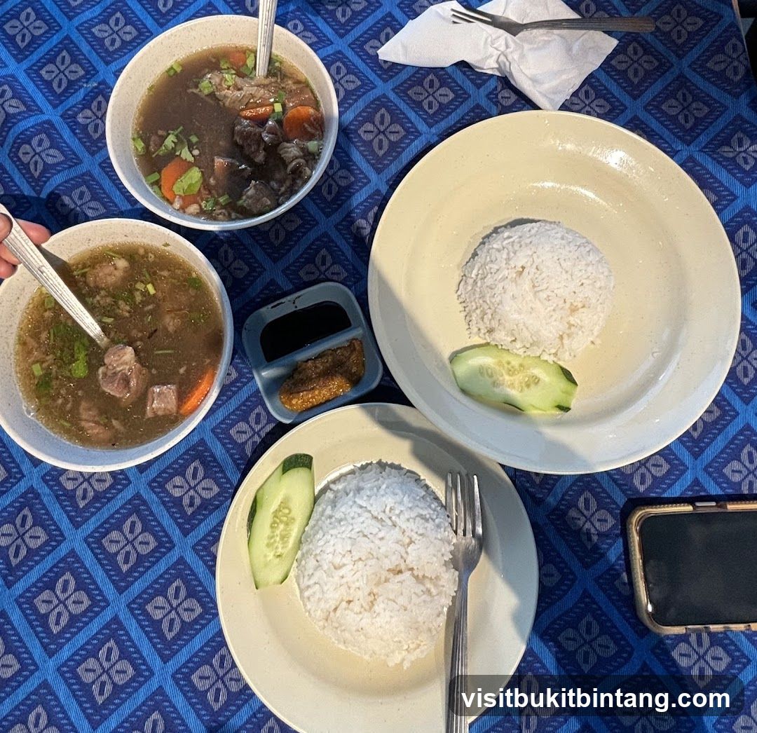 Two bowls of soup with meat and vegetables, and two plates of rice with cucumber slices and a small dish of sauce.
