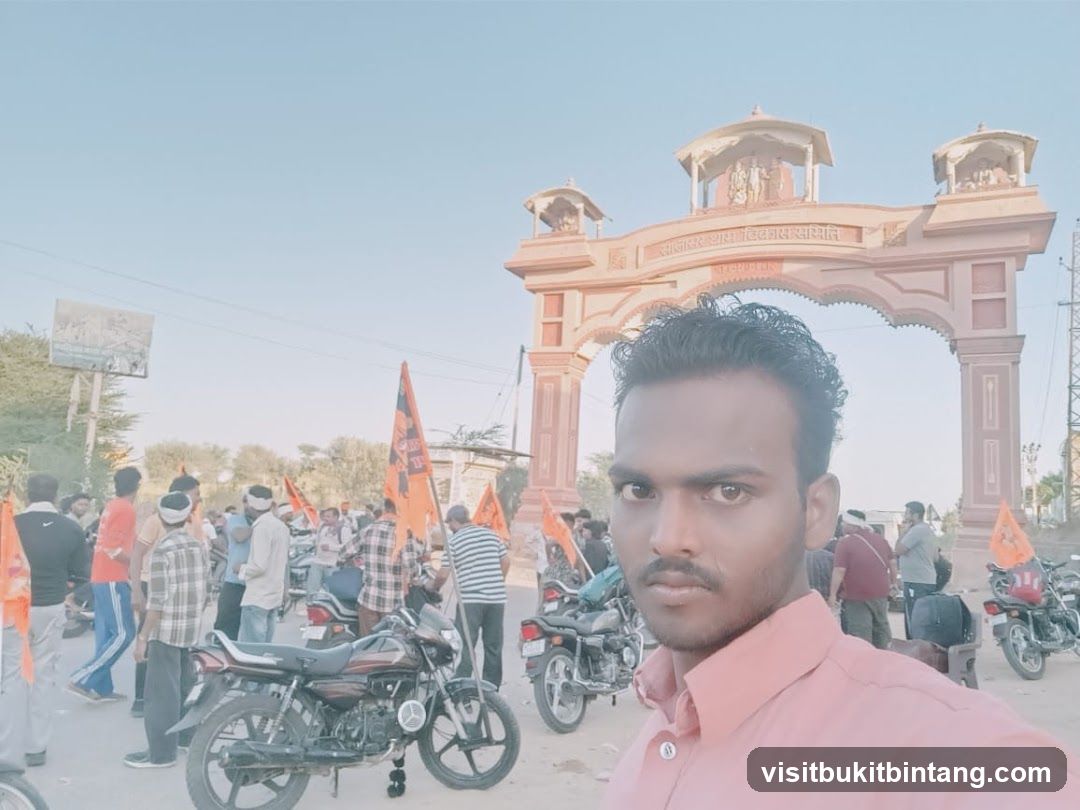 Man taking a selfie in front of a large archway with a crowd and flags