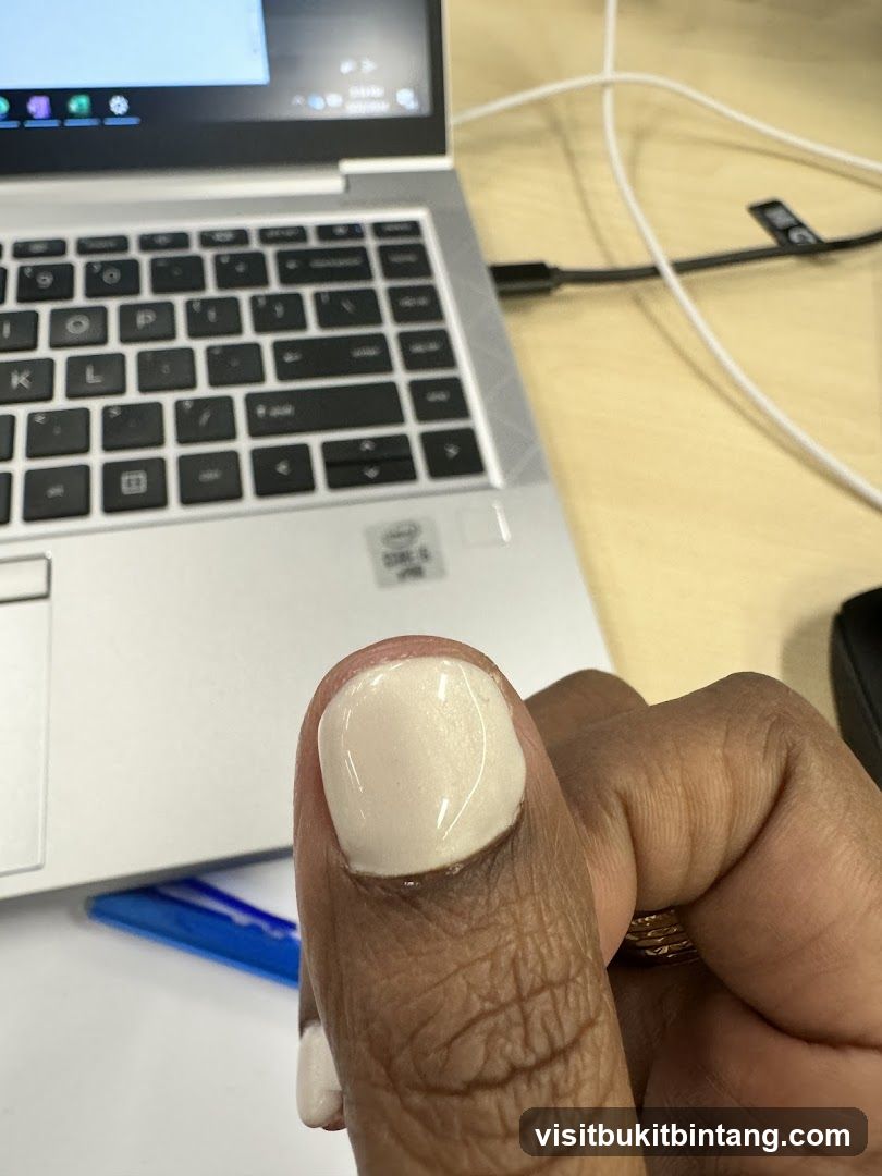 Close-up of a person's thumb with a light-colored nail polish, next to a laptop keyboard.