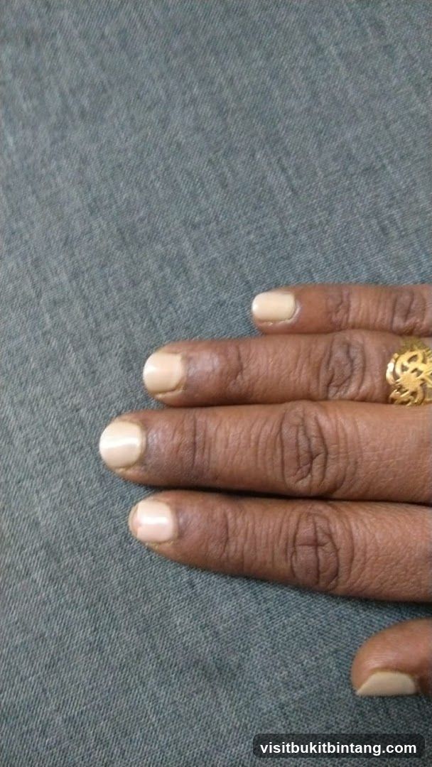 Fingers with light-colored nail polish and a gold ring