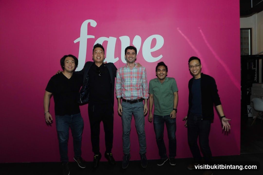 Five men posing in front of a pink wall with a logo