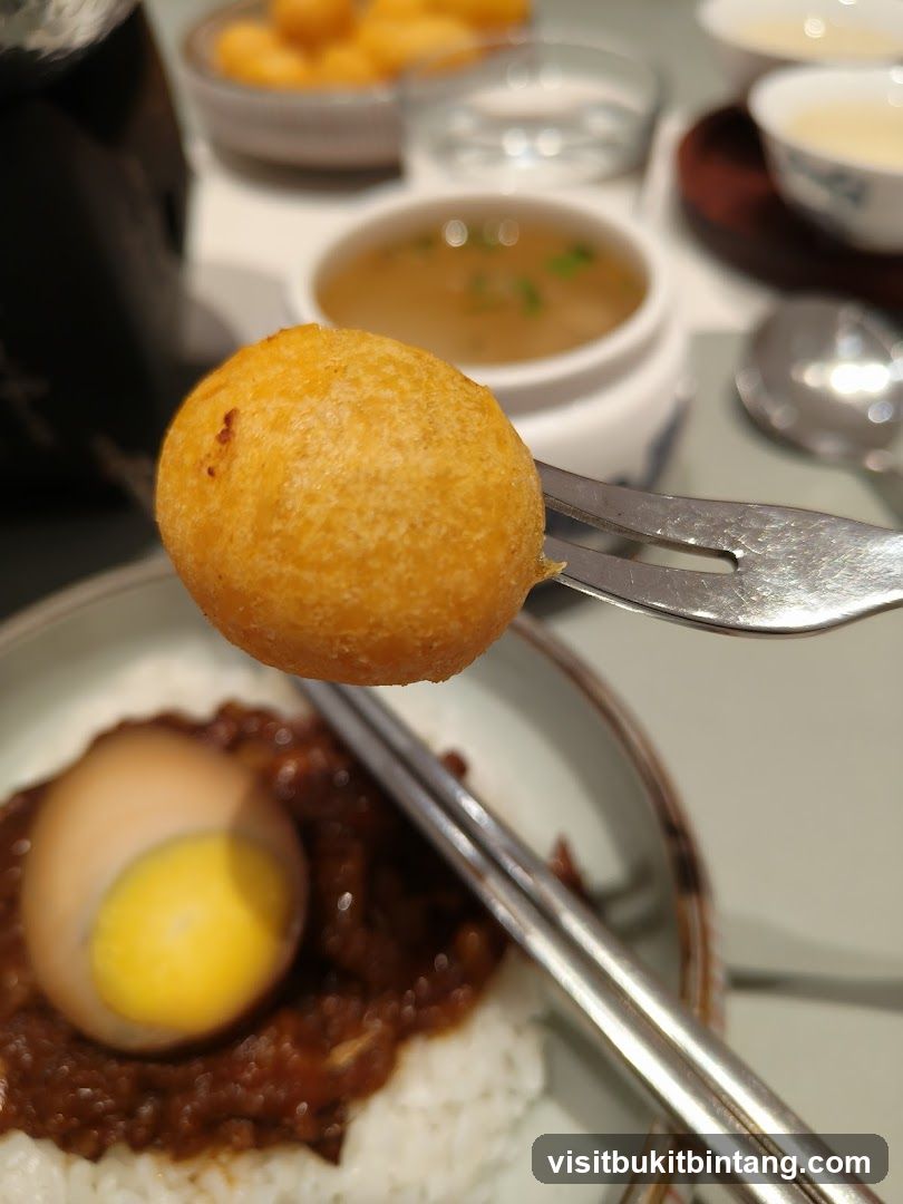 Close-up of a fried ball on a fork over a dish of rice and egg