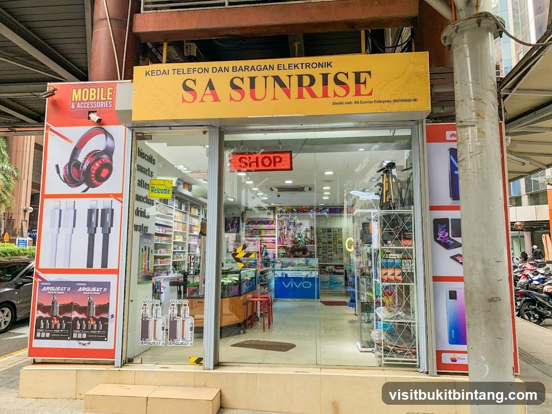 The storefront of SA SUNRISE, a shop selling mobile phones and electronic accessories. The shop has a large glass entrance with various advertisements and product displays visible inside and outside.