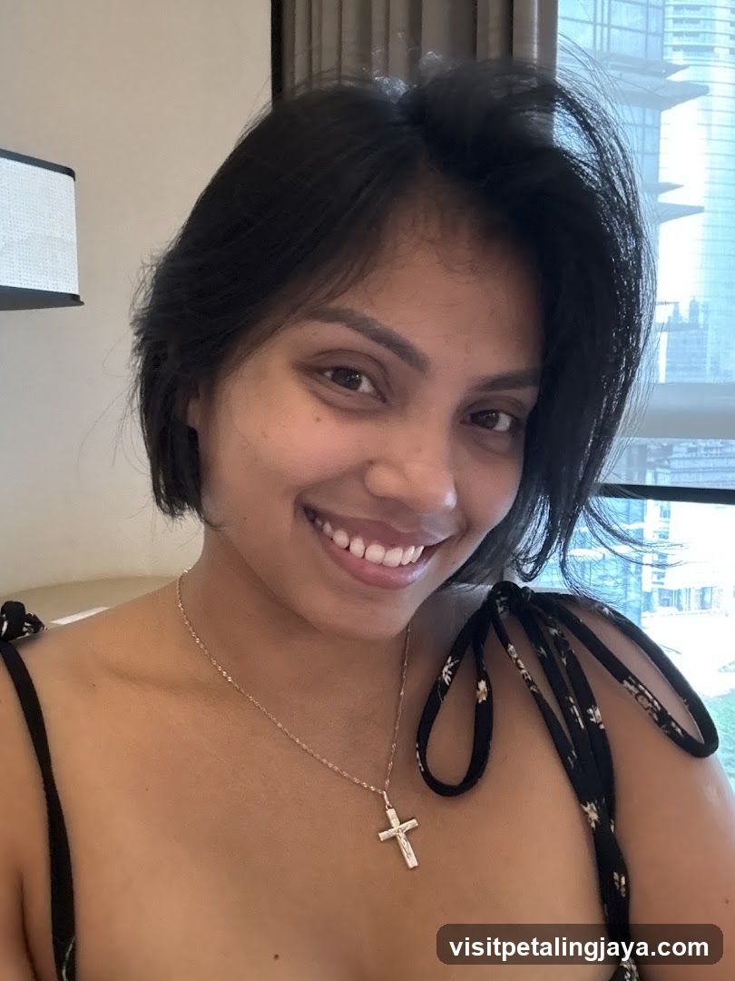 Portrait of a woman with short dark hair smiling at the camera, wearing a necklace with a cross pendant and a black top with floral straps.