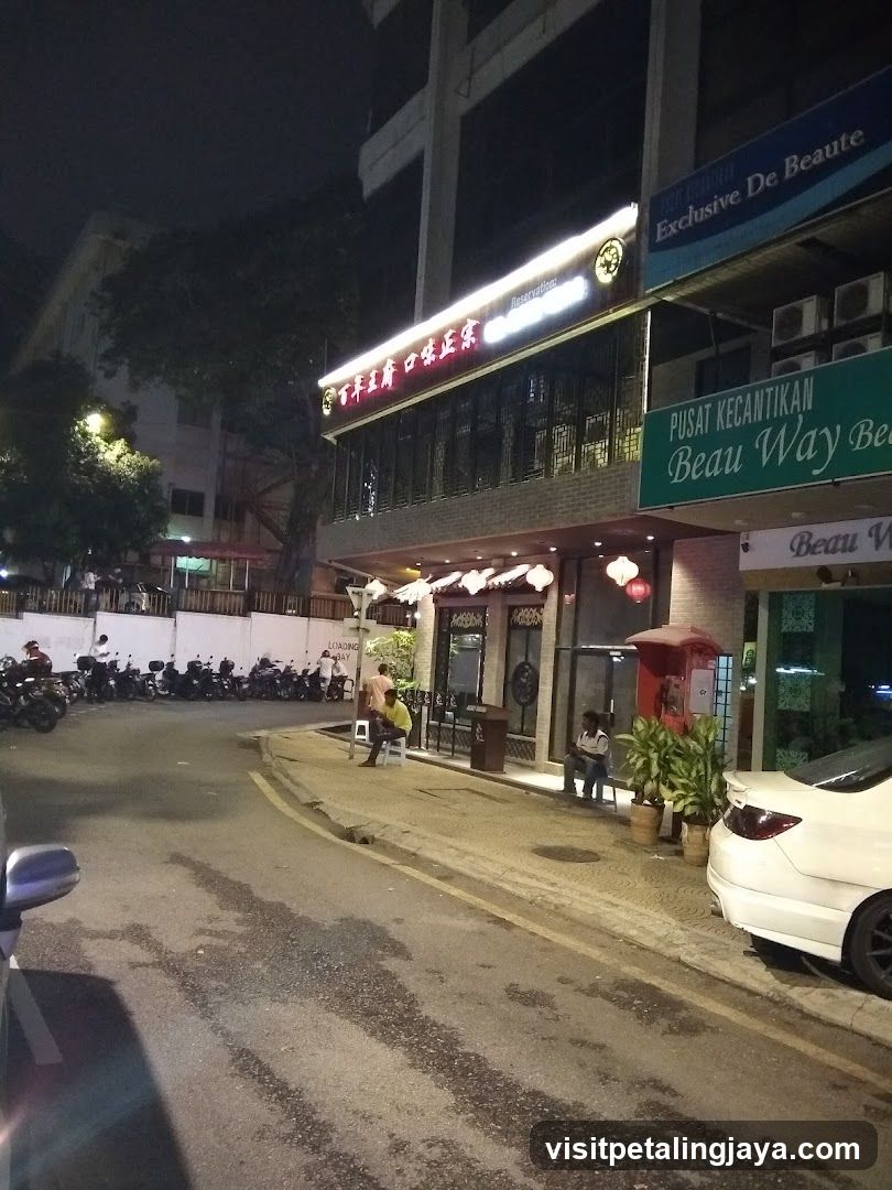 Nighttime street view of storefronts with illuminated signage and parked vehicles.