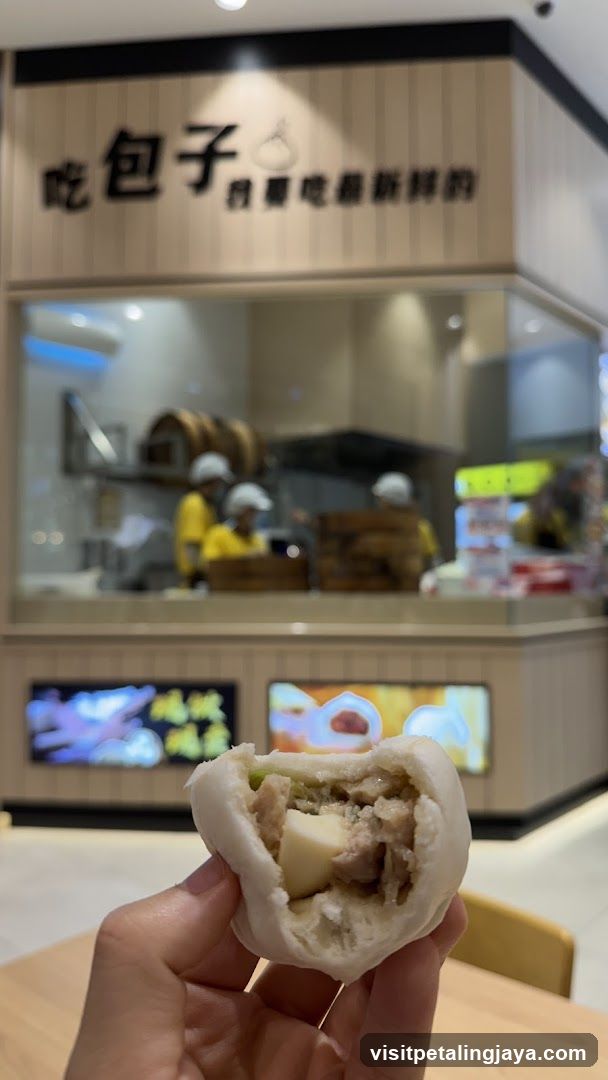 Hand holding a steamed bun in front of a bakery counter
