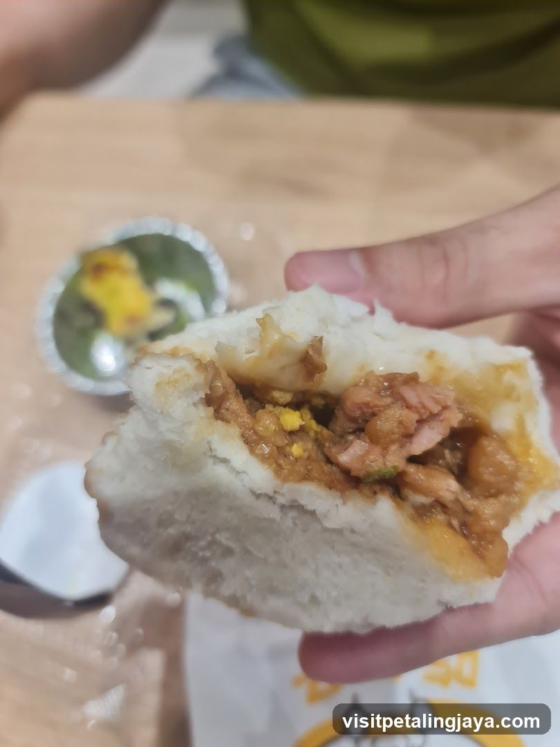 Hand holding a half-eaten bun with savory filling