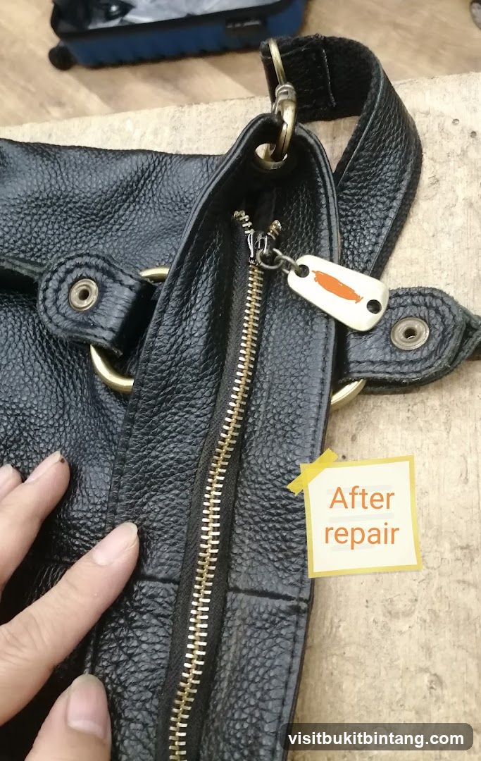 Hand holding a black leather bag with a repaired zipper
