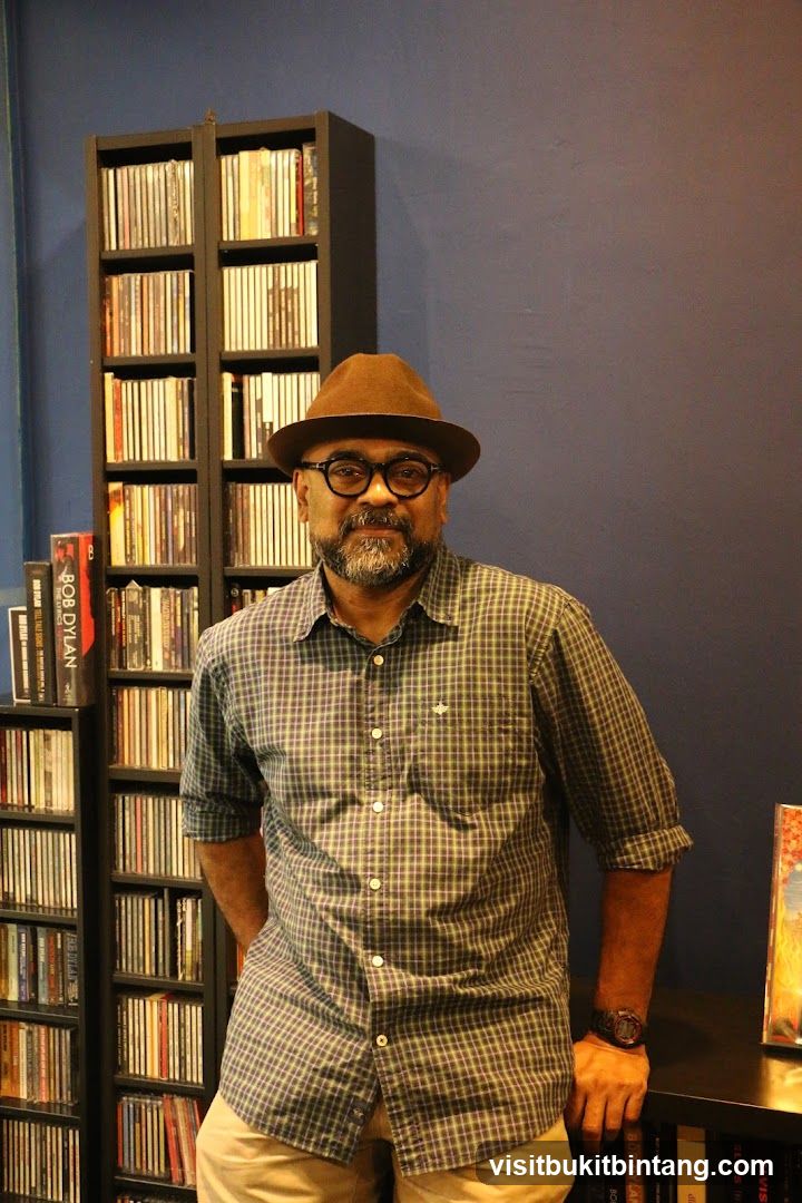 Man in Hat and Plaid Shirt Posed in Front of CD Shelves