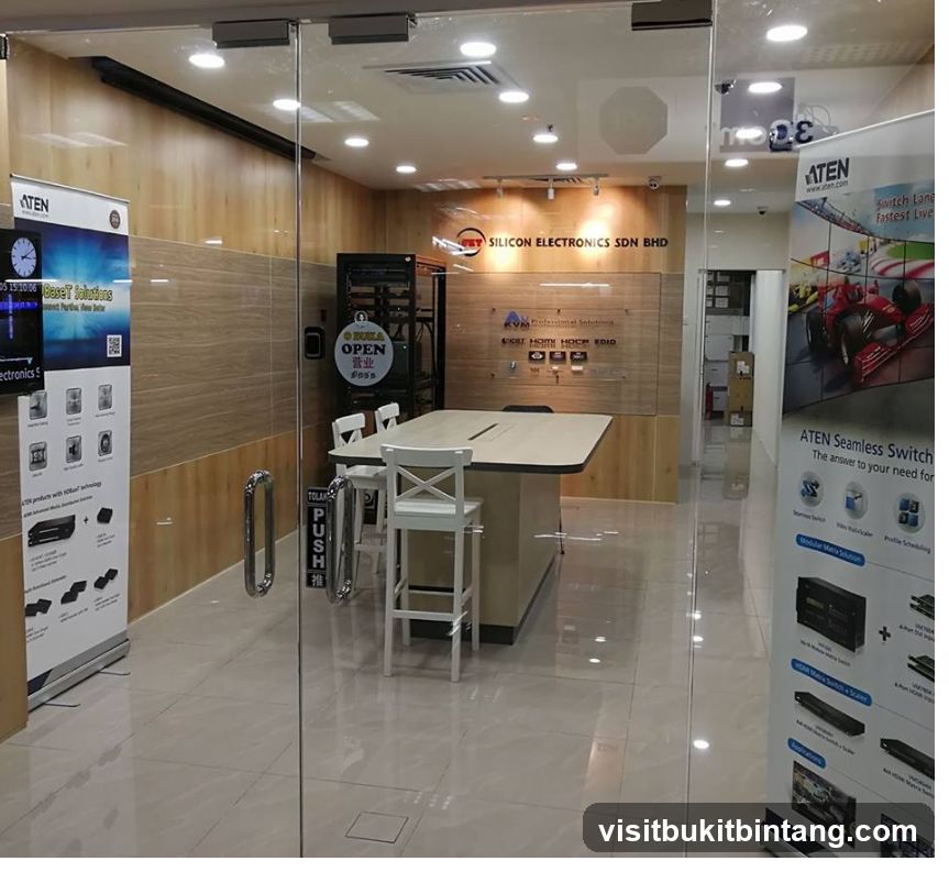 A view through a glass door into a modern office space. The office features a large conference table with chairs, wooden paneling on the walls, and various electronic equipment and displays. Promotional banners for ATEN products are visible on the left and right sides of the entrance.