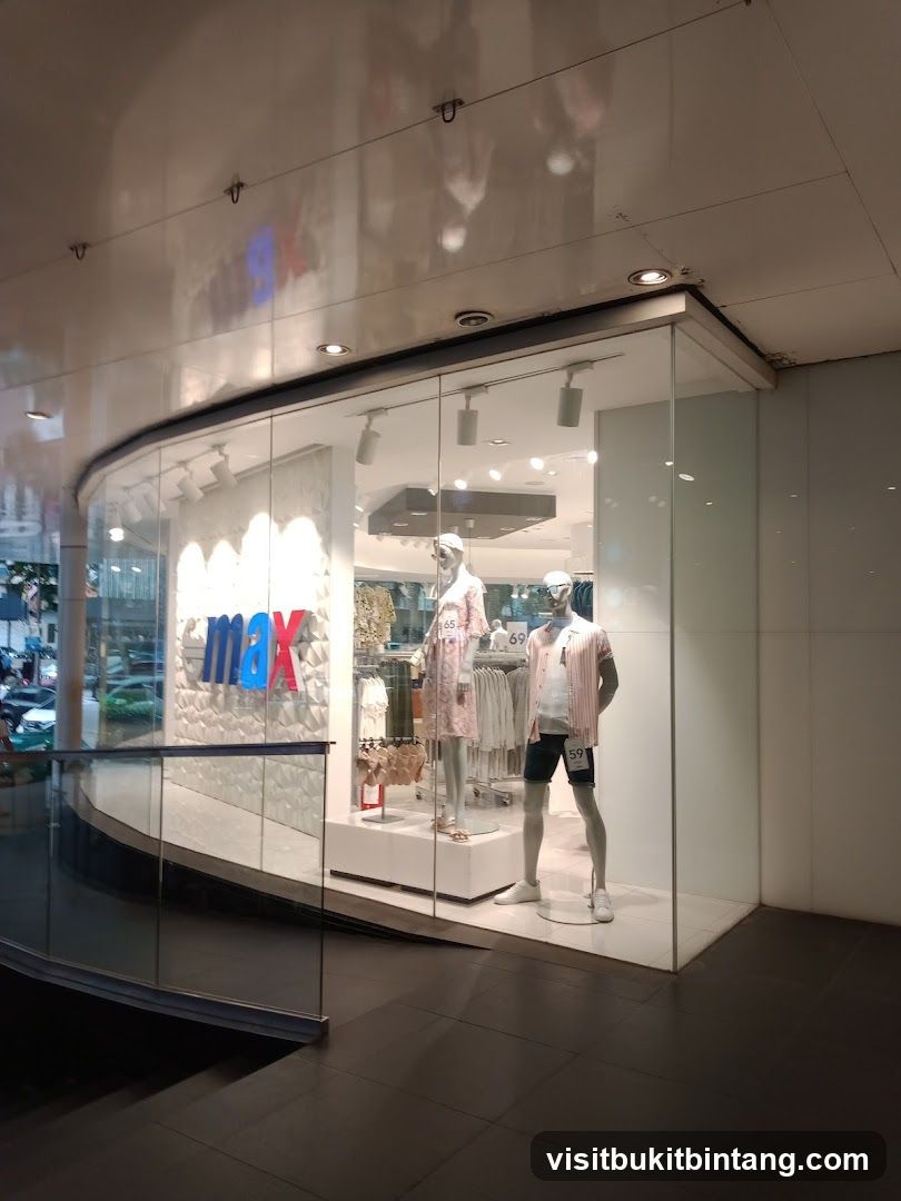 The storefront of an Emax store features a large glass window displaying mannequins dressed in summer clothing. The Emax logo is prominently displayed on the wall behind the mannequins. The store appears to be a clothing retailer.