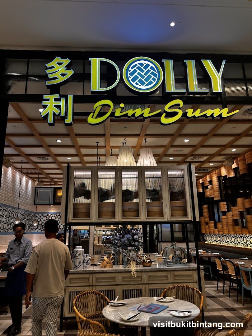 The exterior of a Dolly Dim Sum restaurant. The sign above the entrance reads "DOLLY Dim Sum" in large, illuminated letters. The interior is visible through the entrance, showing tables, chairs, and decorative elements.