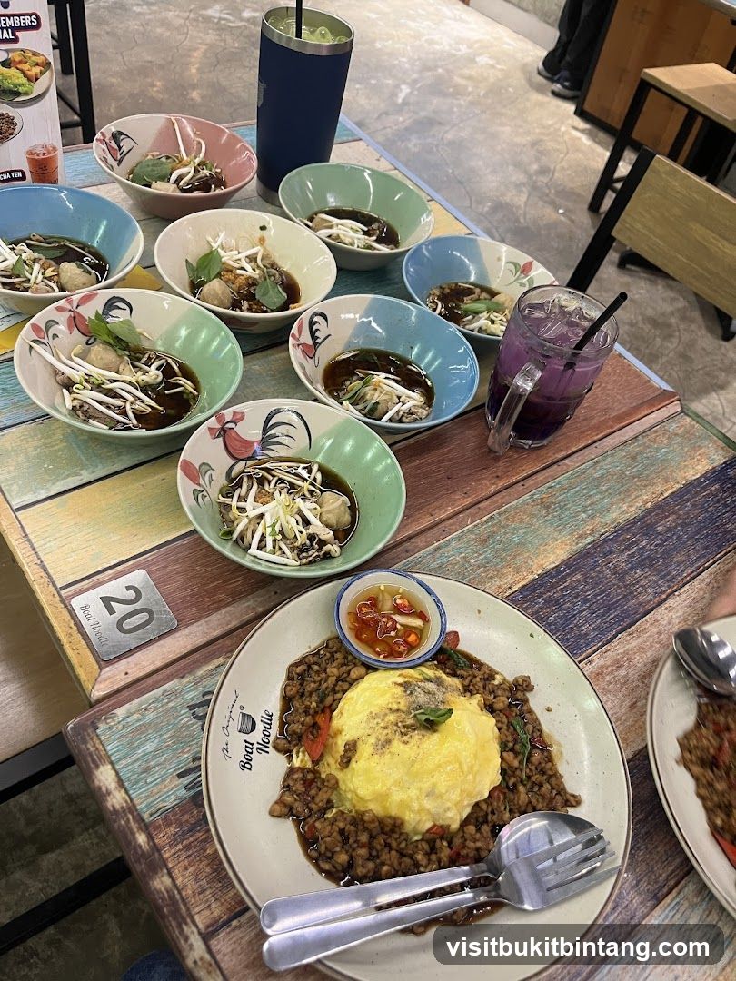 Table with multiple bowls of noodles and a plate of rice with omelet