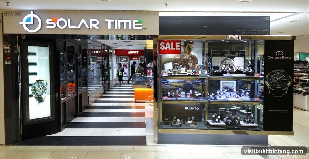 The exterior of a watch store with multiple brands displayed in windows and display cases. The store has a prominent "SOLAR TIME" sign. Inside, there are displays for brands like Cerruti 1881, Esprit, Orient Star, and Suunto. A "SALE" banner is visible.