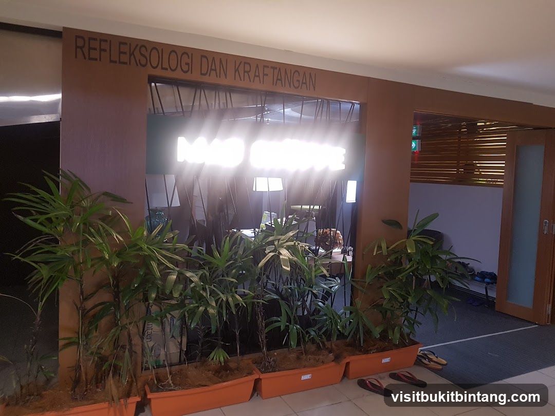 The entrance to a reflexology and handicraft establishment. The words "REFLEKSOLOGI DAN KRAFTANGAN" are visible above a large opening. Inside, a bright sign reads "MAD SENSE". Potted plants are arranged in front of the entrance.