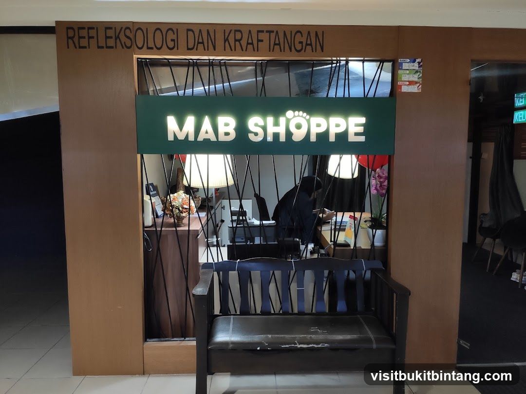 The exterior of a shop called Mab Shoppe, which offers reflexology and hand therapy. The shop has a green sign with white lettering and a foot graphic. There is a wooden bench in front of the entrance.