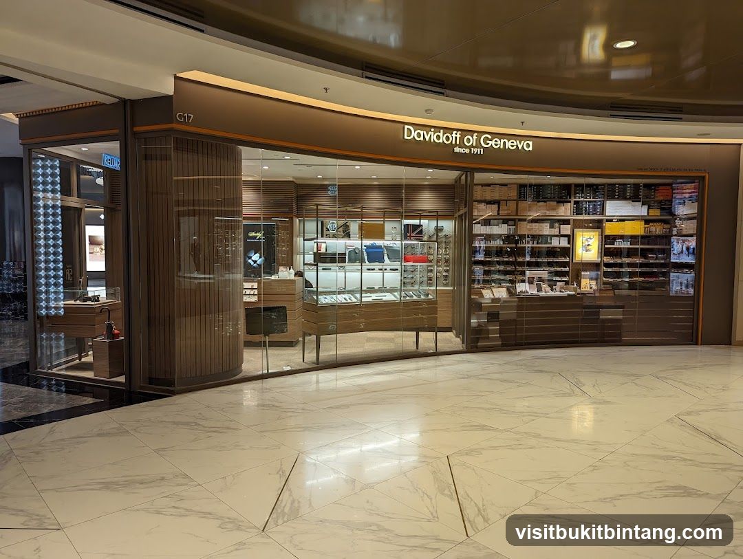 The exterior of a Davidoff of Geneva store, featuring a large glass facade displaying various products. The store's name is prominently displayed above the entrance. Inside, shelves are stocked with boxes of cigars and other merchandise. Display cases showcase watches and accessories. The store is located in a mall with marble flooring.