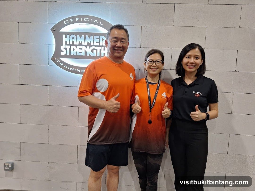 Three people posing in front of a Hammer Strength Training sign