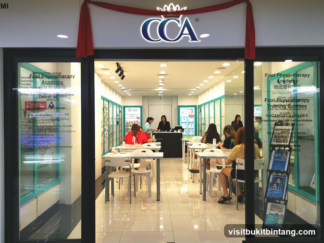 The exterior of a Foot Physiotherapy Academy with the CCA logo above the entrance. Inside, tables and chairs are set up, and several people are seated. The windows display information about operation hours, training courses, and job vacancies.