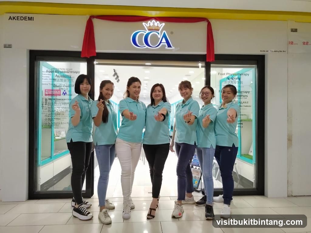 A group of seven women in light blue polo shirts stand in front of the entrance to the CCA Foot Physiotherapy Academy. The academy's logo, CCA with a crown above it, is visible on the facade. Signs inside the window display information about the academy, including operation hours and courses offered.