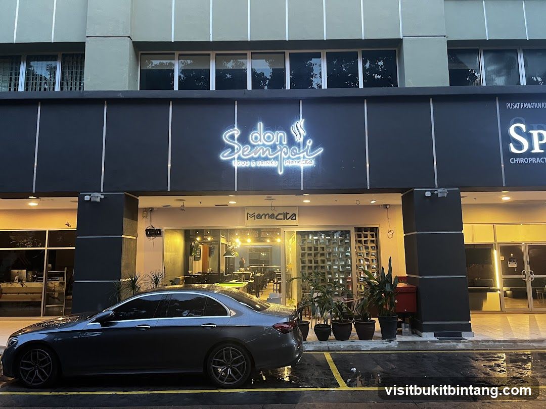 The exterior of a restaurant called Don Sempoi Food & Drink. The restaurant has a neon sign above the entrance. There is a car parked in front of the restaurant.