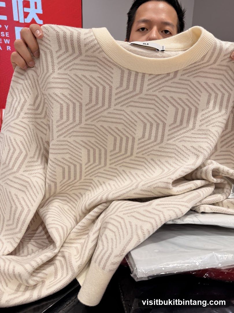 Man holding a cream-colored sweater with a geometric pattern