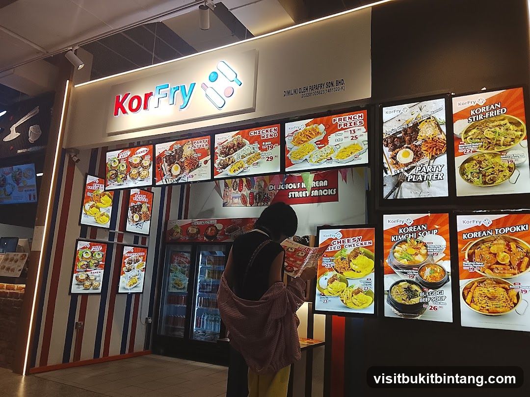 A KorFry storefront with illuminated menu boards displaying Korean street food. A person is looking at a menu.