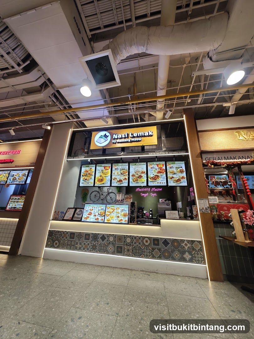 A food stall with a prominent sign displaying "Nasi Lemak by Memang Meow" and a cartoon cat logo. The stall features digital menu boards showcasing various dishes, a decorative bicycle, and a counter area. The lower part of the stall is adorned with patterned tiles.