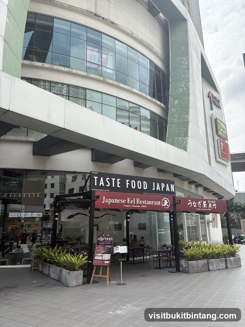 The exterior of a Japanese Eel Restaurant called Taste Food Japan. The restaurant has an outdoor seating area with tables and chairs. There are plants in planters in front of the restaurant. The restaurant has a large sign with the name of the restaurant and "Japanese Eel Restaurant" written on it. There is also a smaller sign with Japanese writing.