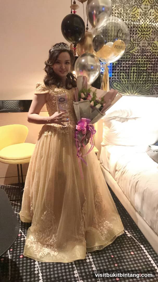 Woman in a formal gown holding a trophy and flowers