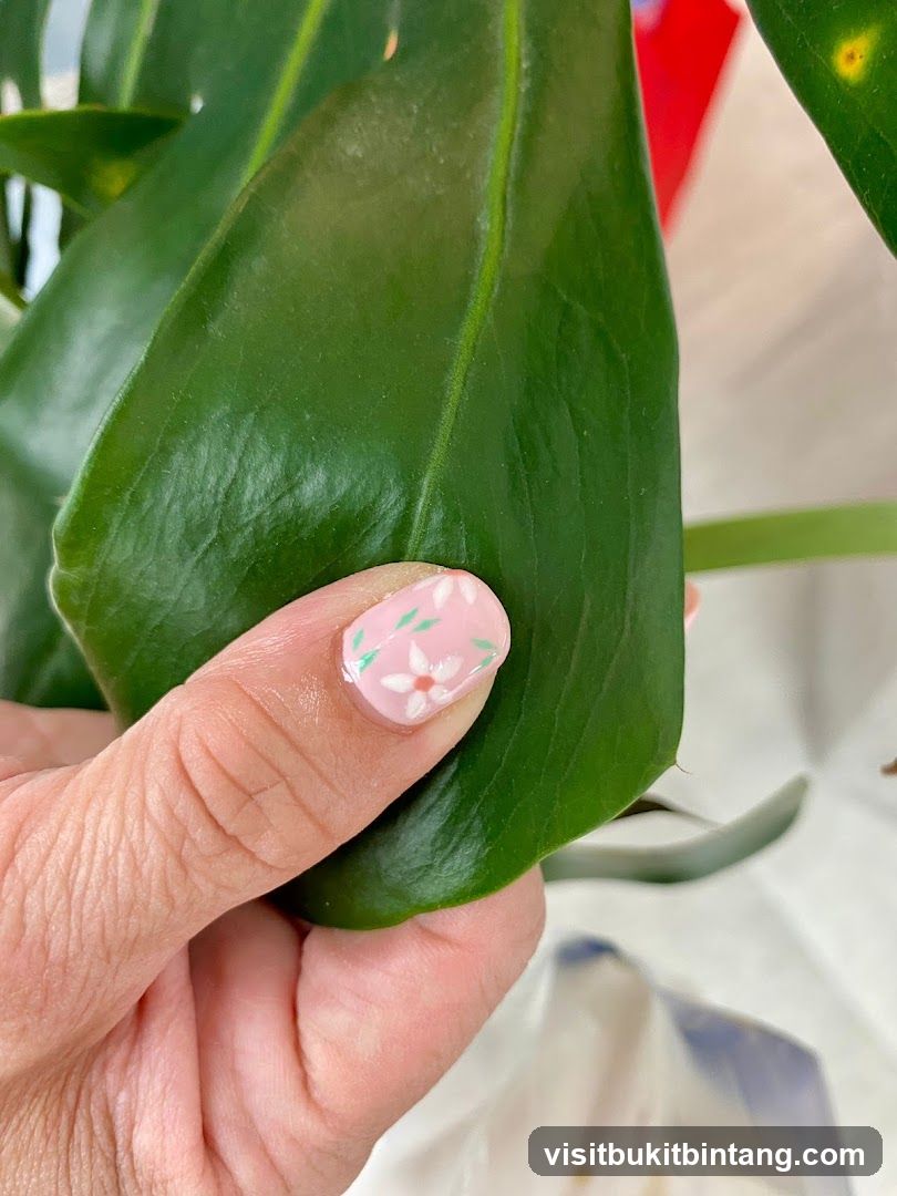 Close-up of a hand with floral nail art touching a large green leaf